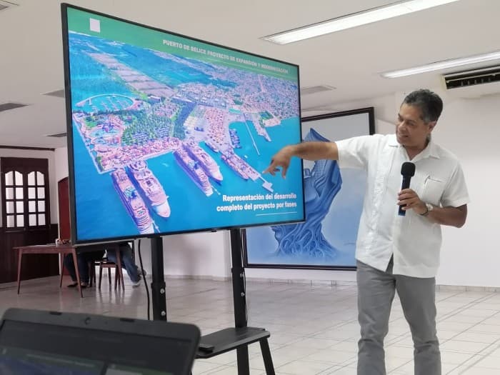 Presentador señala un mapa digital del puerto de Belice durante una exposición sobre la expansión y comercialización del proyecto portuario.