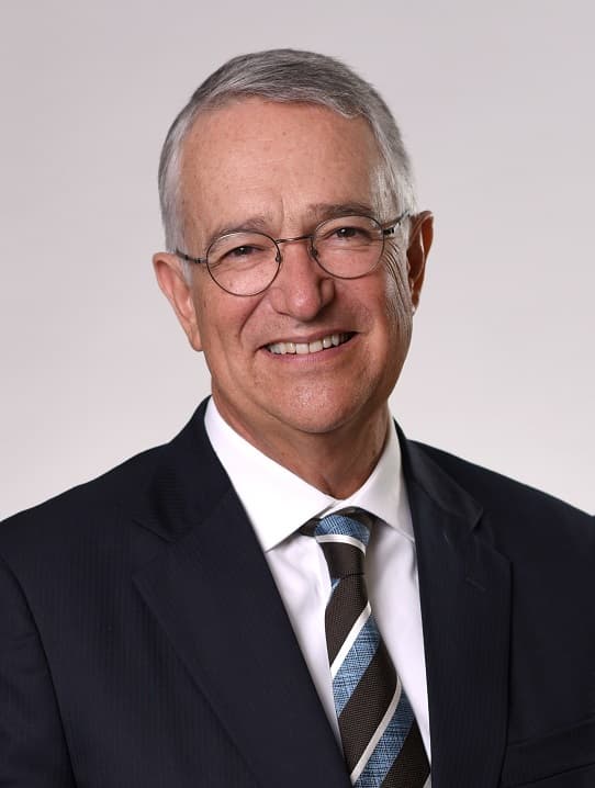 Retrato profesional de un hombre mayor con lentes y traje oscuro sonriendo a la cámara.