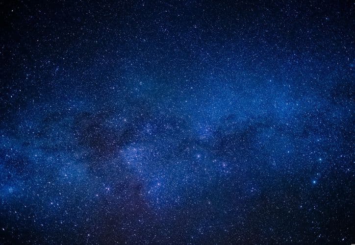 Cielo nocturno estrellado con la Vía Láctea visible como una banda luminosa azul atravesando el firmamento lleno de estrellas.