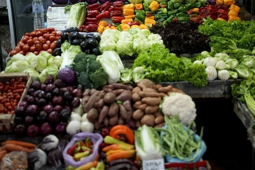 Puesto de verduras y productos frescos en un mercado con tomates, lechugas, chiles, papas, cebollas y otras hortalizas organizadas por secciones.