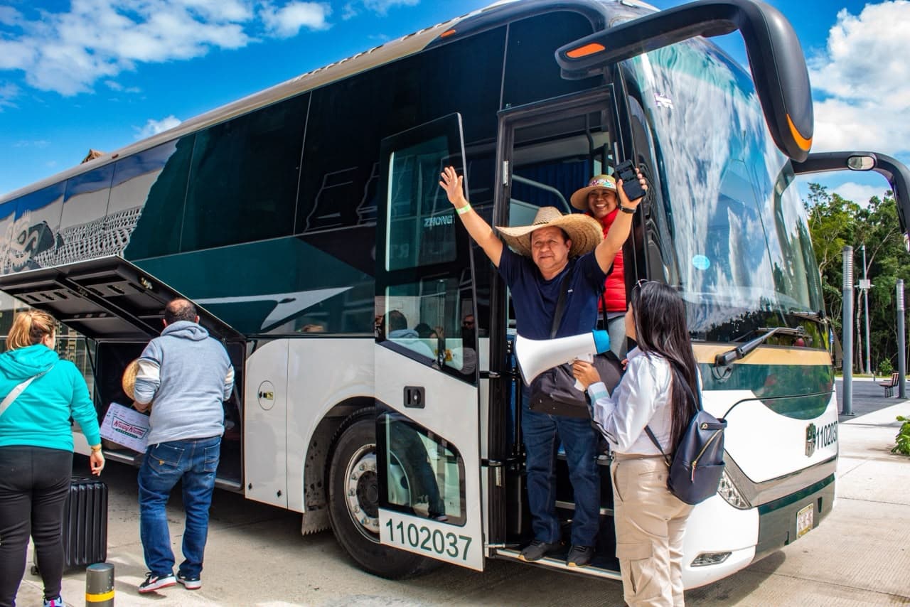 Pasajeros suben a un autobús de transporte con número de placa visible, bajo cielo despejado, en una terminal de movilidad.